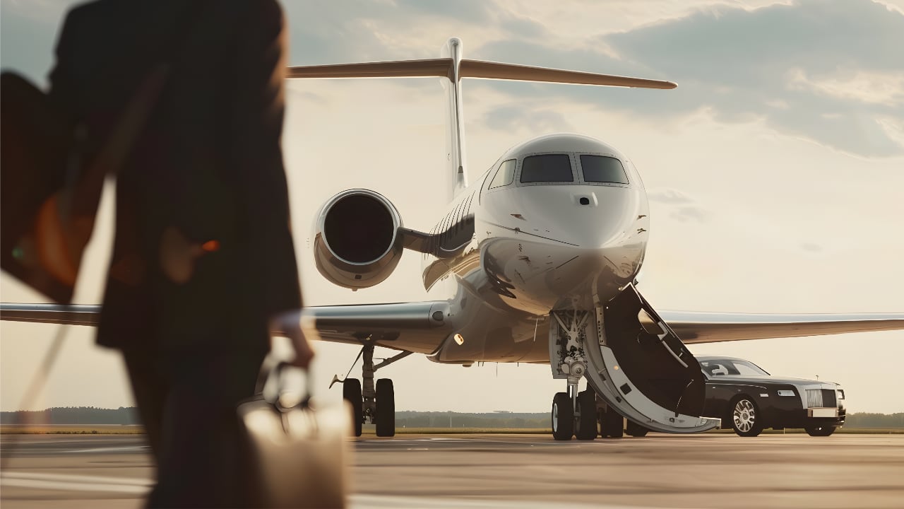 Partial view of a man in a suit holding a suitcase, with a white private jet in focus behind him.