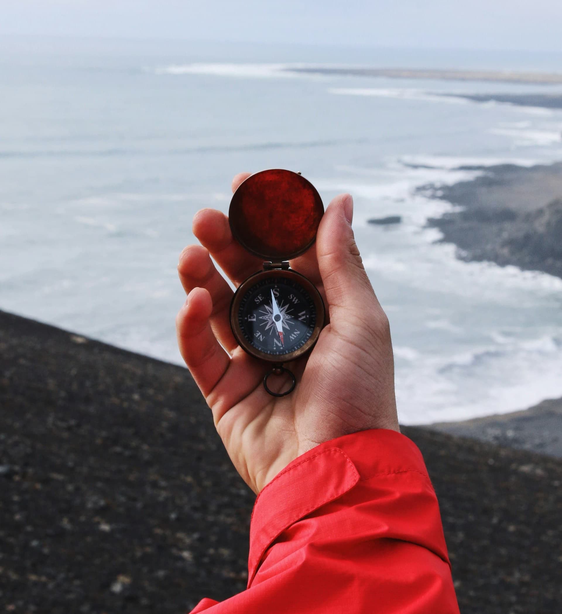 hand in the foreground holding a compass, facing an open ocean horizon.